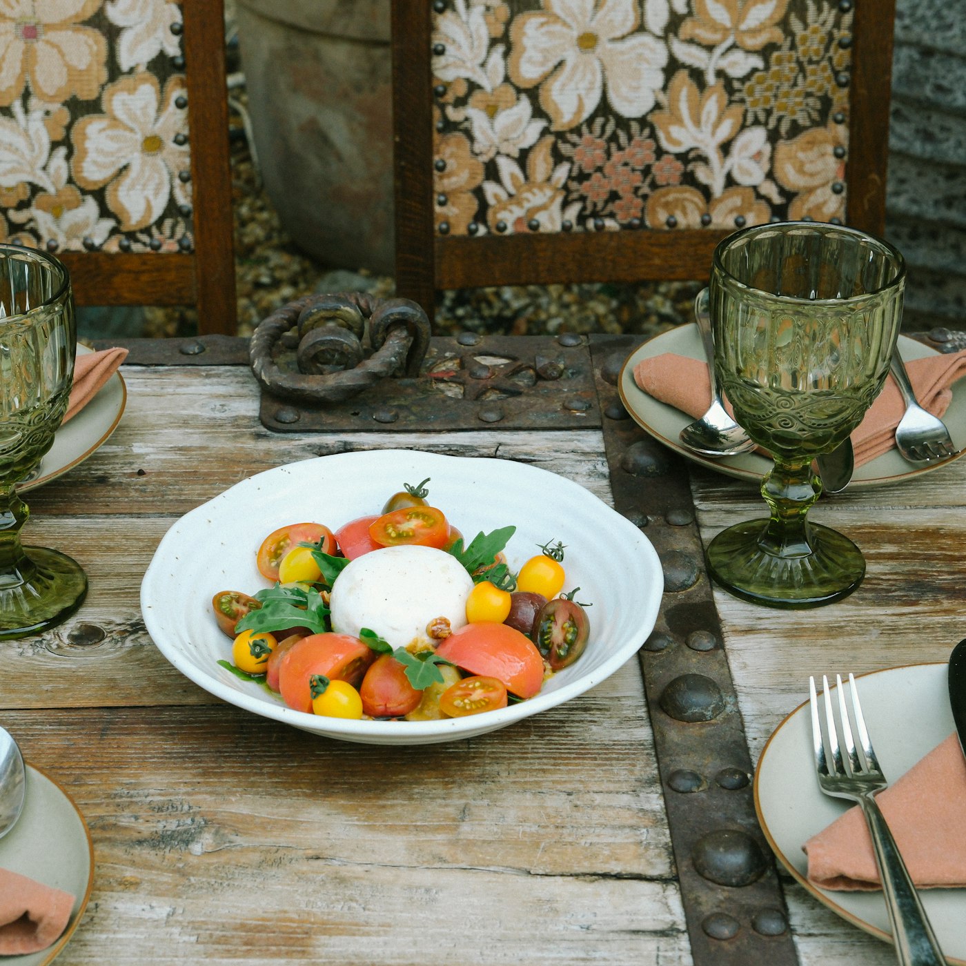 A table set outside with burrata, tomatoes and green glasses