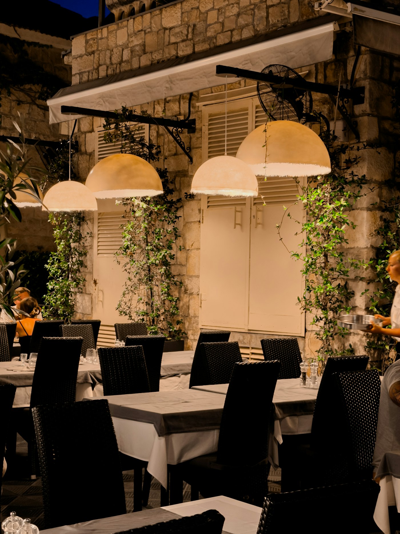 The stone terrace of Chez Lina at dusk, tables set under the lamps