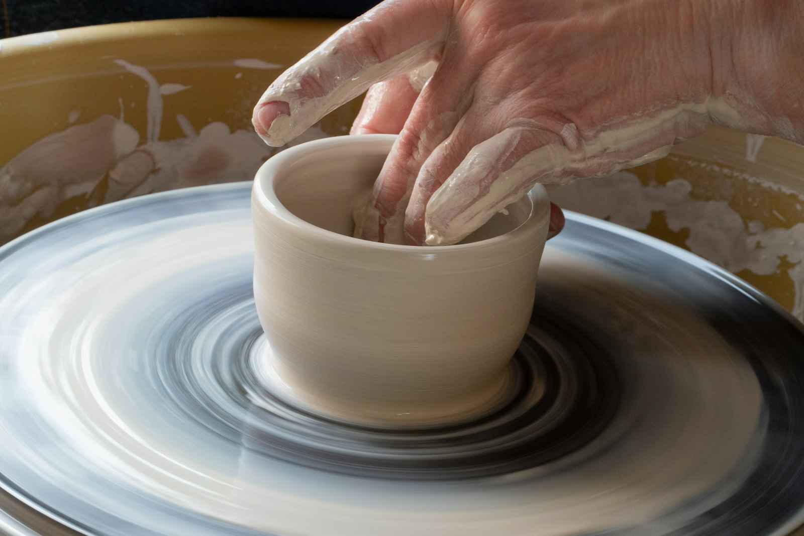 Two hands shaping a pot on a turning wheel